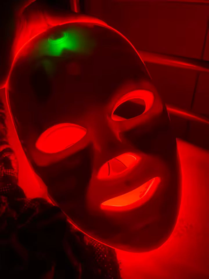 Customer wearing the Red Light Therapy Mask with red light glowing in a dark setting.